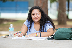 Female writing outside at table.