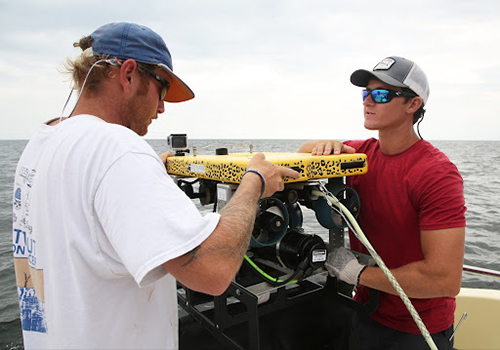 Two students working on boat doing research.