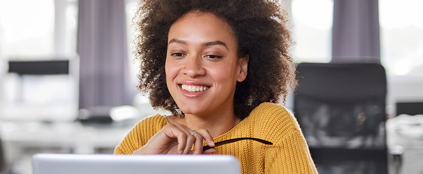 Student looking at laptop smiling holding glasses