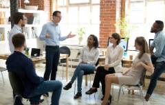 Man standing talking to a group of people sitting.